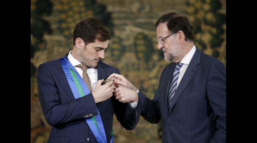 Spanish goalkeeper Iker Casillas and Spain's Prime Minister Mariano Rajoy attempt to hang the Grand Cross of the Royal Order of Sporting Merit on Casillas' jacket at the Moncloa Palace in Madrid
